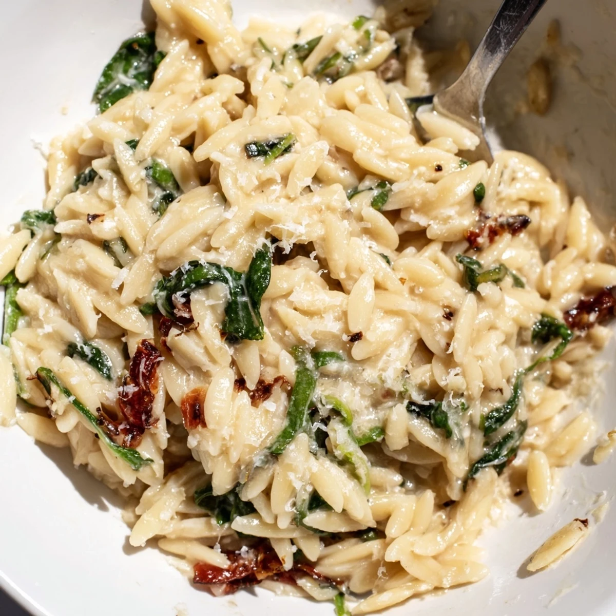 Creamy Tuscan Orzo Bowl with sun-dried tomatoes and wilted spinach, drizzled with olive oil.  