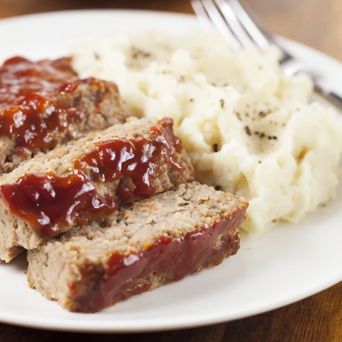 Comforting Classic Meatloaf & mashed potatoes garnished with fresh parsley and savory glaze.  