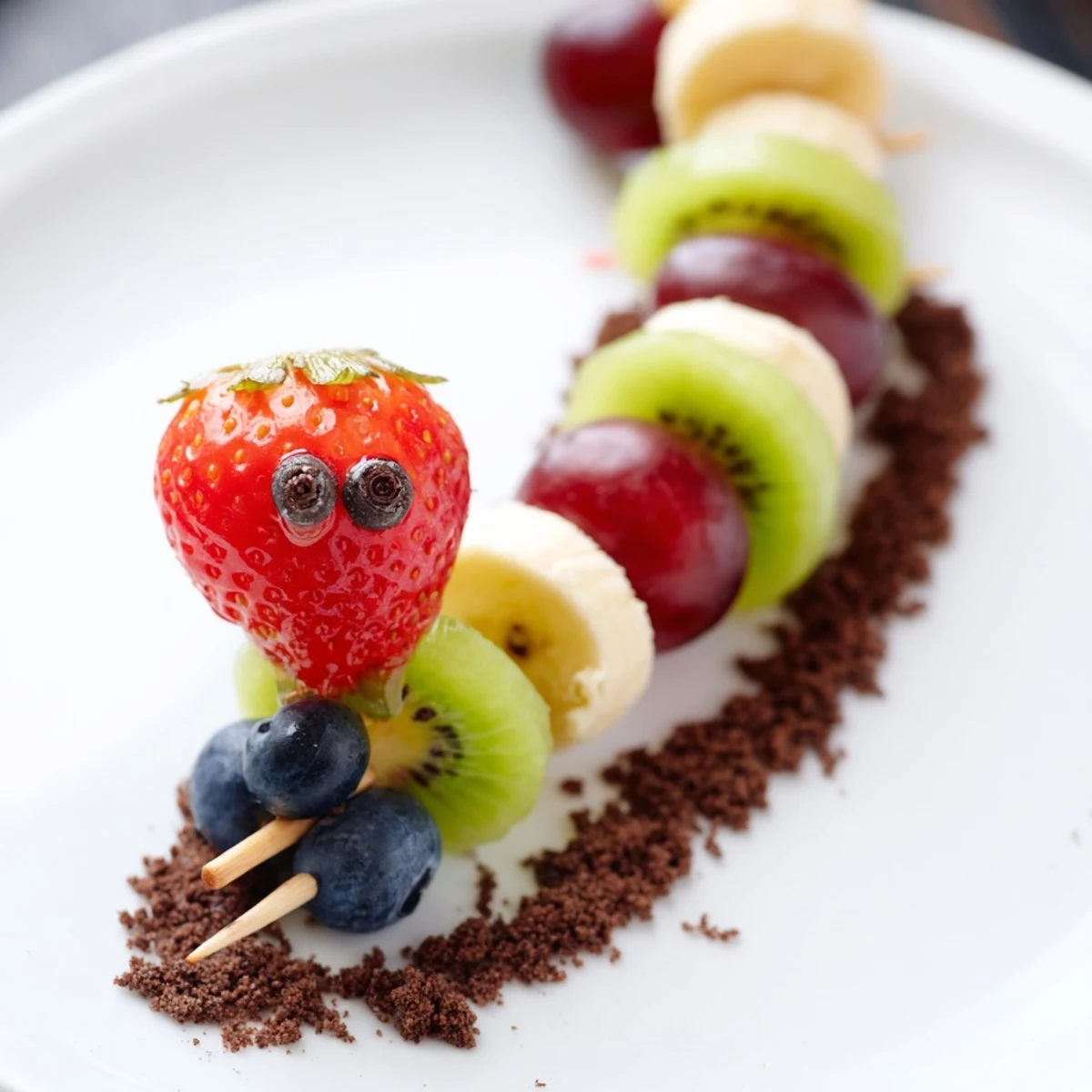 Vibrant Caterpillar Fruit Skewer Track: a healthy and fun snack with colorful fruit caterpillars and cookie crumbs.