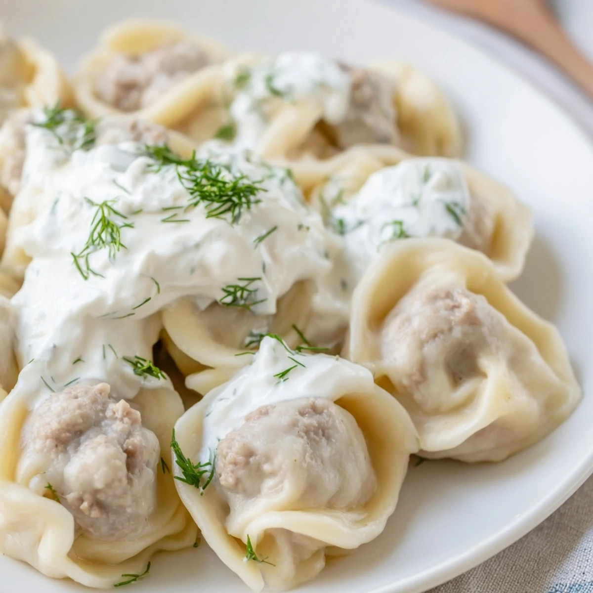 Steaming hot Russian pelmeni, tender meat dumplings, are pictured with cool sour cream.