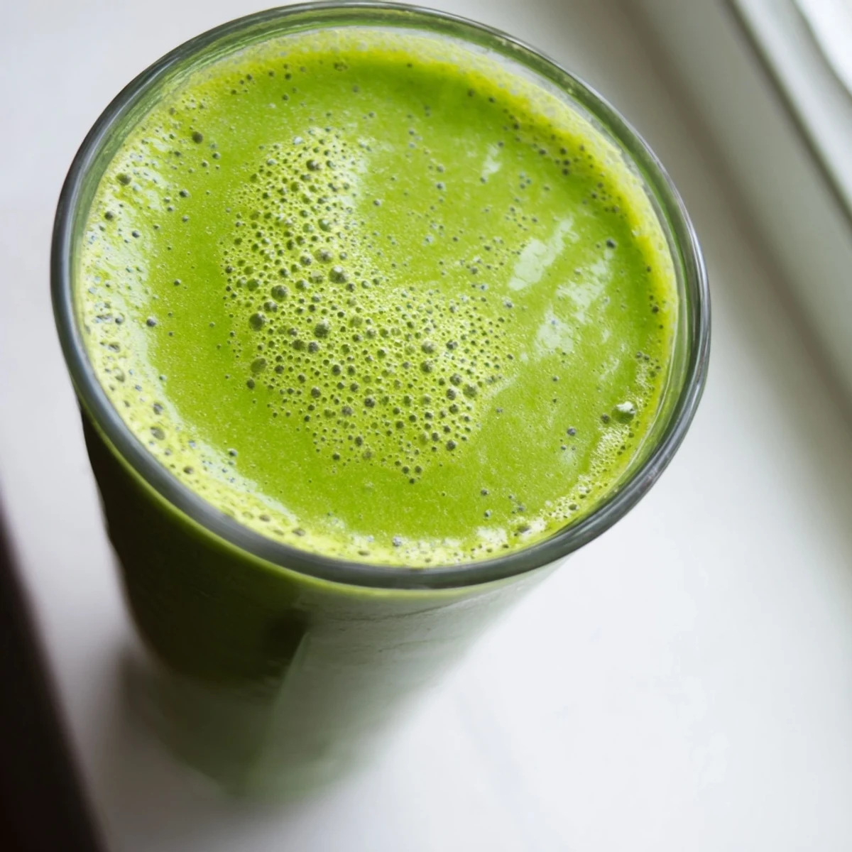 A vibrant green Spinach-Hidden Smoothie in a tall glass, with mango and pineapple chunks visible for a refreshing breakfast treat.