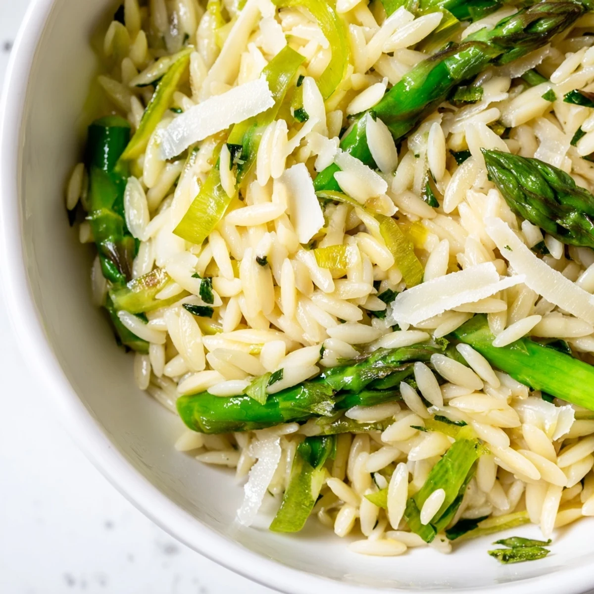 Bright spring Asparagus Lemon Orzo Salad tossed with arugula and herbs, served on a light ceramic plate near a lemon wedge.