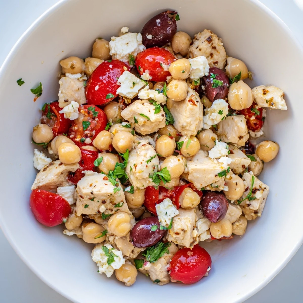 A close-up of Mediterranean Chickpea Chicken Salad with juicy chicken, crumbled feta, and halved cherry tomatoes on a rustic platter.