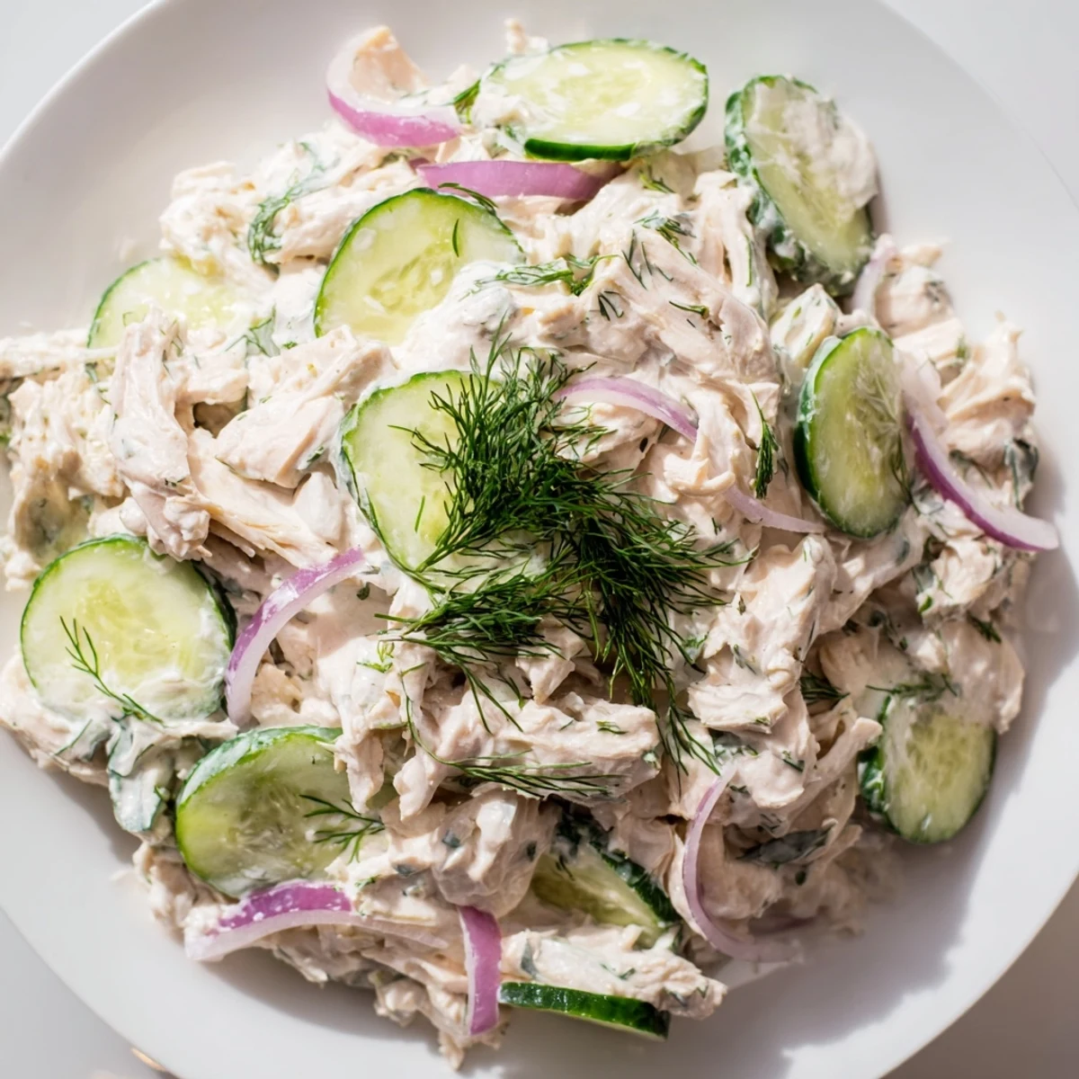 Creamy cucumber chicken salad served in a white bowl, garnished with green onions and lemon wedges, perfect for a refreshing high-protein lunch.