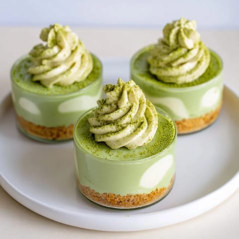 These no-bake Matcha Swirl Snowdrift Cheesecake Cups show a beautiful, layered dessert with a lovely green hue.