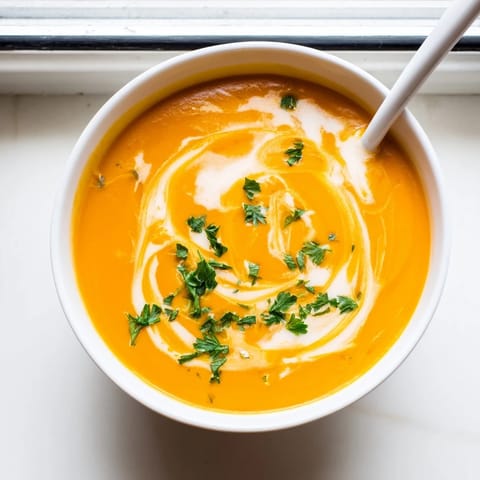 Velvety carrot-based soup served hot in a rustic bowl beside crusty bread.  