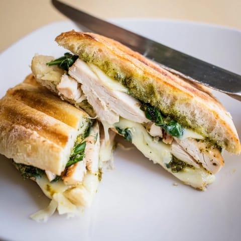 Sliced Chicken Pesto Panini revealing layers of grilled chicken, vibrant spinach, and juicy tomato on ciabatta.  