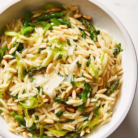 A white bowl holds the Asparagus Lemon Orzo Salad with grated Parmesan and toasted pine nuts, topped with fresh parsley.