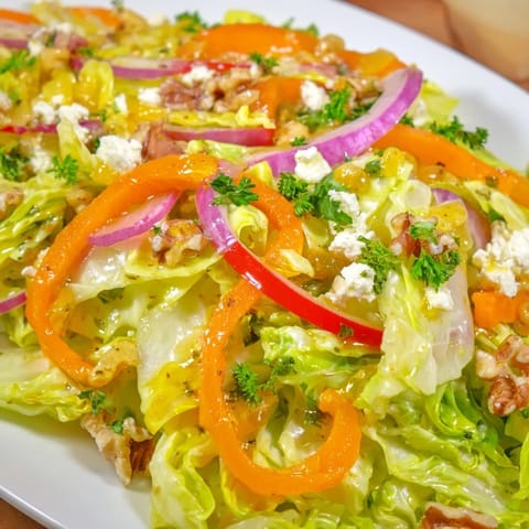 Bright, steaming Cooked and Loved Cabbage Salad topped with crumbled feta and toasted walnuts on a rustic serving plate.