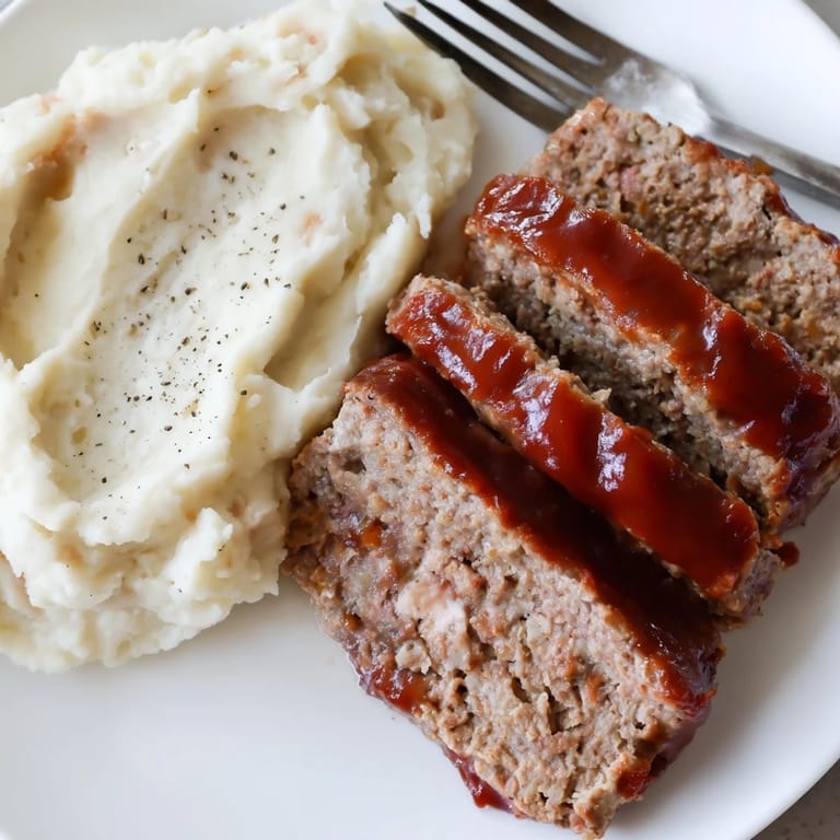 Sliced Classic Meatloaf & mashed potatoes drizzled with rich brown sugar ketchup glaze.