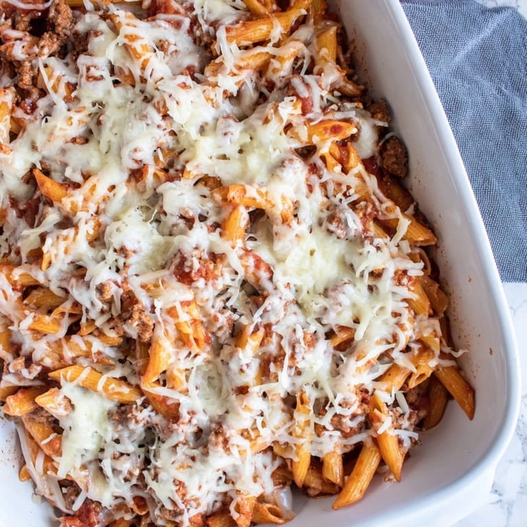 A close-up shot of a steaming Cheesy Beef & Penne Bake, showing melted cheese and bubbling tomato sauce.