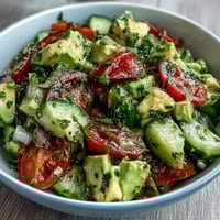A vibrant cucumber tomato avocado salad with lemon dressing, bursting with fresh flavors and colorful ingredients.  